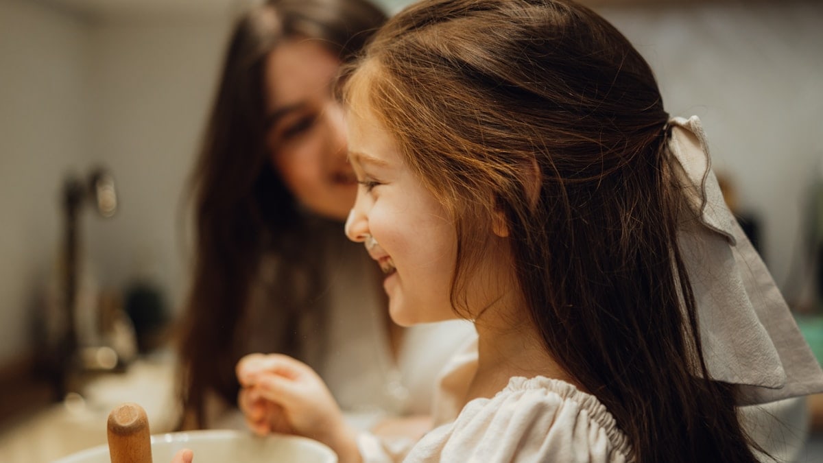 A little girl sitting in front of a sink next to a woman